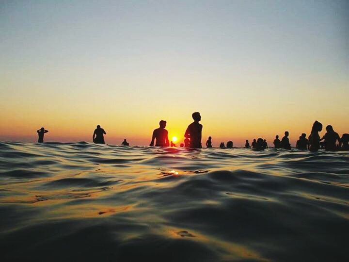 water, sunset, clear sky, sea, beach, copy space, leisure activity, waterfront, orange color, shore, lifestyles, reflection, sand, men, vacations, large group of people, person, enjoyment, silhouette