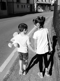 Rear view of siblings holding hands walking on sidewalk in city