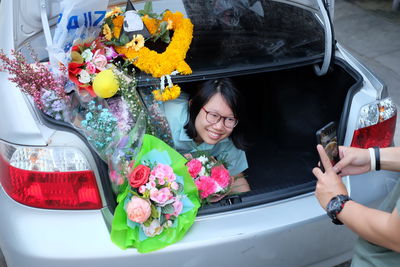 Cropped hands photographing happy young woman with bouquet in car trunk