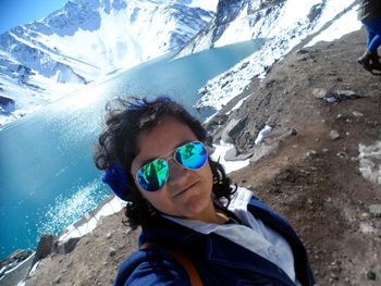 Portrait of woman wearing sunglasses at lakeshore against snowcapped mountains