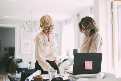 Two women standing at workplace in living room working at home