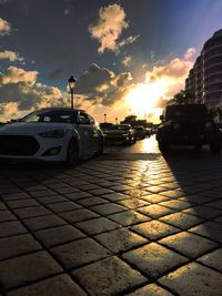 Cars on city street against sky during sunset