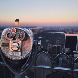 Close-up of coin-operated binoculars with cityscape in background during sunset