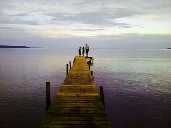 People on pier over sea against sky