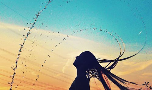 Silhouette woman splashing water with hair against sky during sunset
