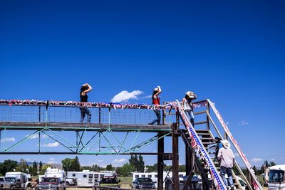 People wearing cowboy hats walking on bridge over parking lot against blue sky