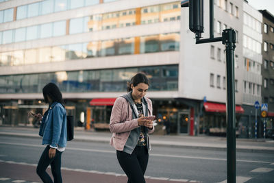 Females walking on sidewalk while using smart phone against building in city