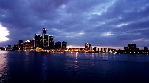 Calm sea with illuminated buildings against clouds