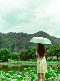 Rear view of woman with umbrella standing against sky
