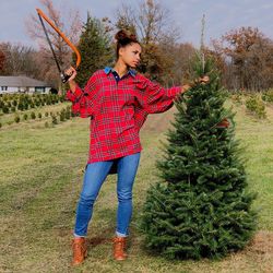 Teenage girl with hand saw standing by tree on grassy field