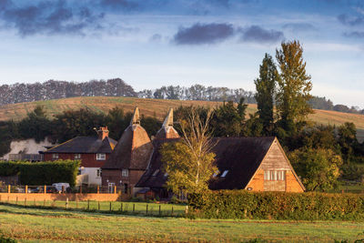 House on field by trees and houses against sky