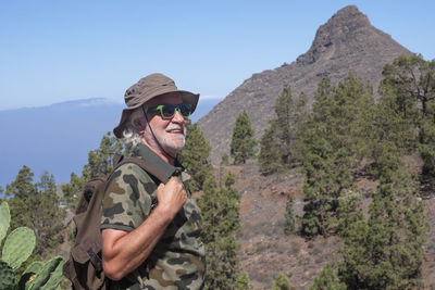 Low angle view of senior man looking away standing against mountain