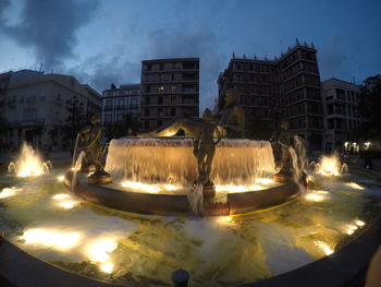 Fountain in city against sky at night