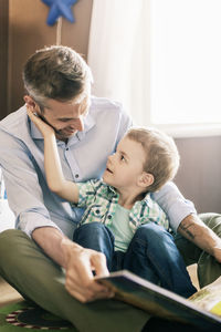 Happy father reading book to son while sitting on floor at home