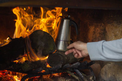Close-up of hand holding kettle in fireplace