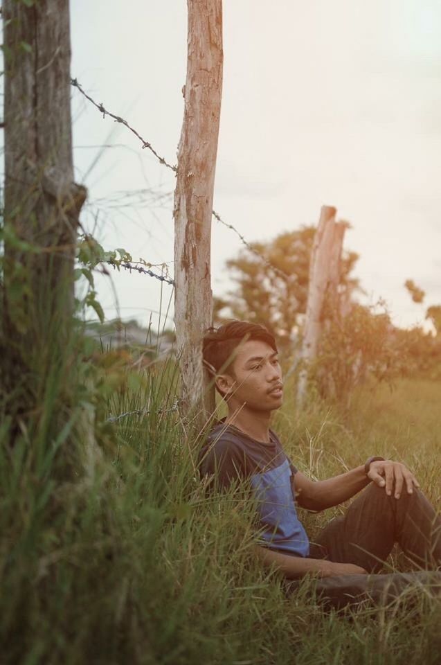 SIDE VIEW OF A BOY SITTING ON FIELD