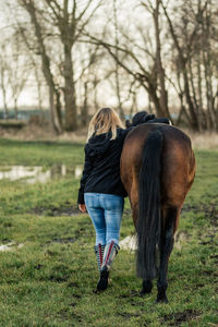 Rear view of woman walking with horse on field