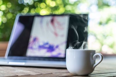 Close-up of coffee cup by laptop on table