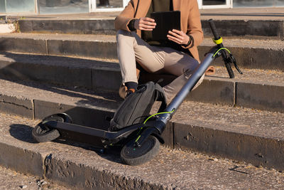 Cropped unrecognizable man working on his tablet sitting in stairs with electric scooter 