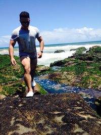 Young man walking on rock by sea against sky