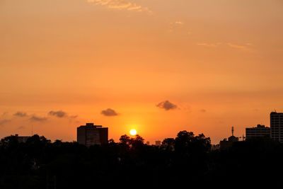 Silhouette trees and buildings against orange sky during sunset