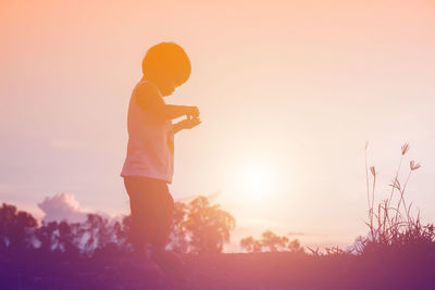 Side view of silhouette man standing on field against sky during sunset