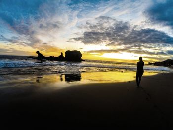 Silhouette person standing on beach against sky during sunset