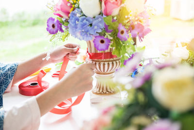 Cropped hands of woman tying ribbon on vase at home