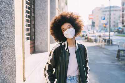 Curly hair woman with protective face mask standing on footpath