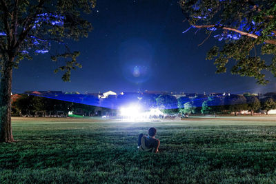 Man lying on illuminated grassy field against sky at night