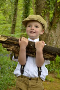 Low angle view of cute boy holding firewood while standing in forest