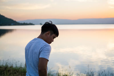 Side view of boy looking at sea against sky during sunset