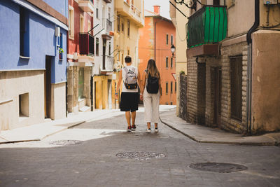 Rear view of couple holding hands walking on street amidst buildings