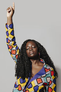 Pensive african american woman with curly hair in stylish african outfit standing on white background. she is with eyes closed pointing finger up