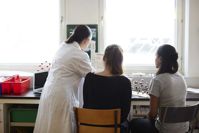 Rear view of mature chemistry teacher with young students in classroom