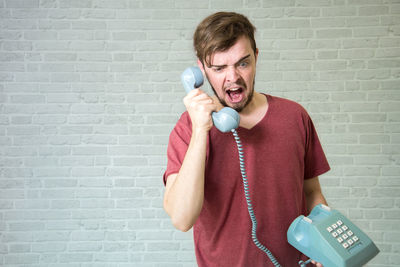 Portrait of man holding mobile phone against wall