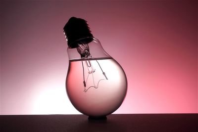 Close-up of liquid in light bulb on table against pink background