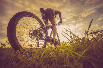 Low angle view of mature man riding bicycle on grassy field against cloudy sky