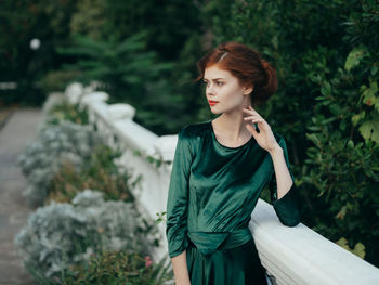 Young woman looking away while standing against plants