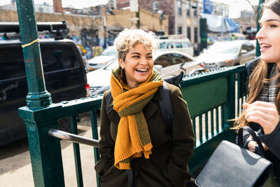 Cheerful woman with friend talking while walking on sidewalk at city