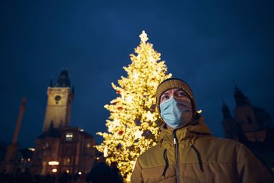 Low angle of man against illuminated christmas tree at night