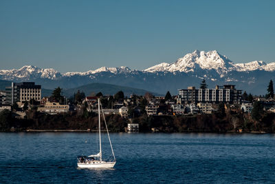 Sailboats in sea by buildings against sky