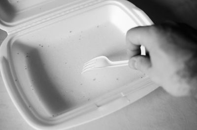 Male hand with a white plastic fork and an empty foam container for food.