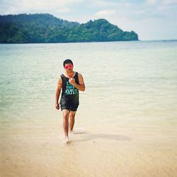 Young man walking on shore at beach against sky during sunny day