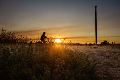 Silhouette man on field against sky during sunset