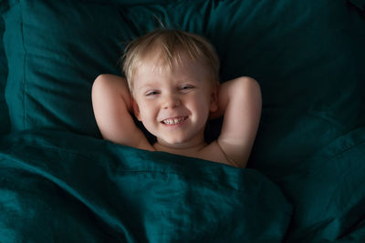 The baby blond woke up and lies laughing and smiling on green bedding. 