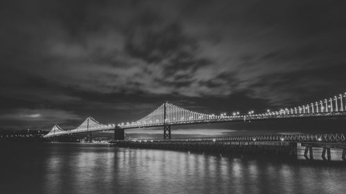 Suspension bridge over river against cloudy sky