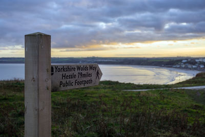 Information sign on land by lake against sky during sunset