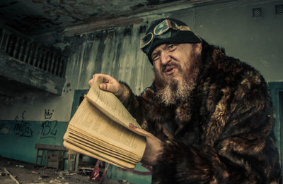 Mature man holding book while talking in messy old house