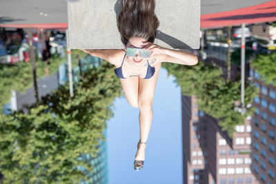 Portrait of young woman wearing sunglasses and bikini while lying on road in city during sunny day